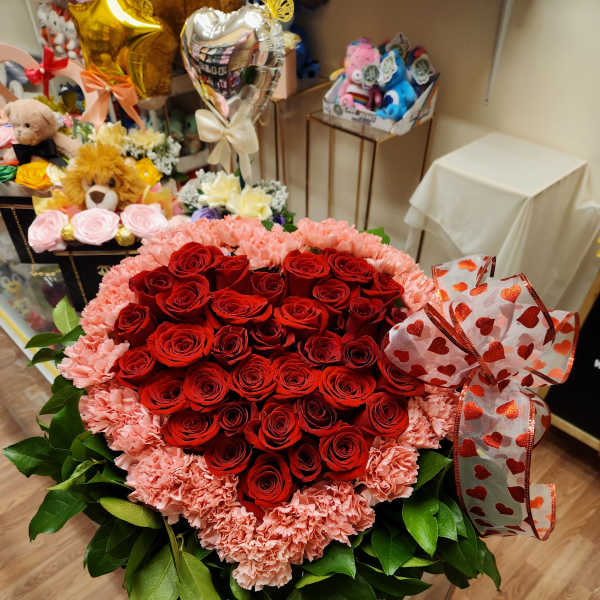 Heart-shaped bouquet of red roses and pink carnations with a heart ribbon