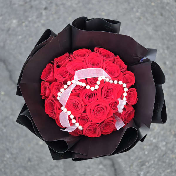 Bouquet of red roses wrapped in black paper with a white ribbon