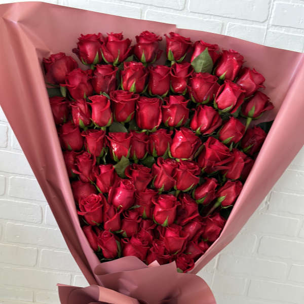 Large bouquet of red roses wrapped in pink paper with a striped ribbon