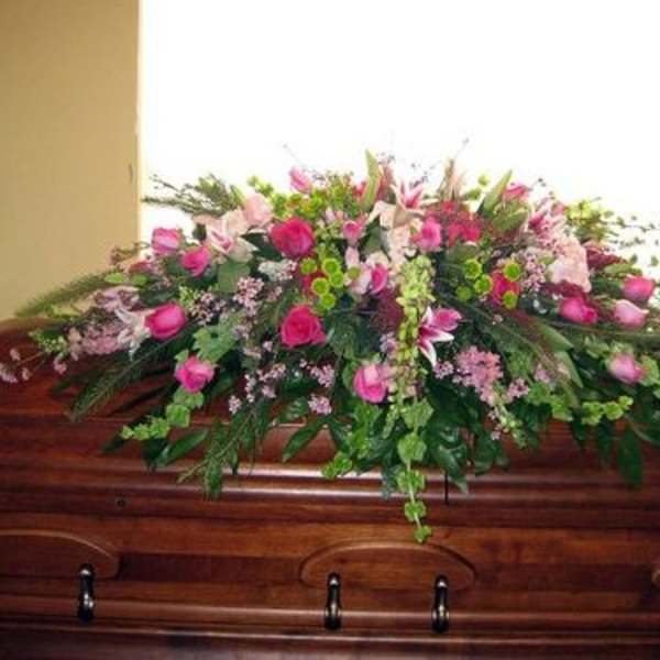 Pink and green casket spray arranged on a polished wooden casket