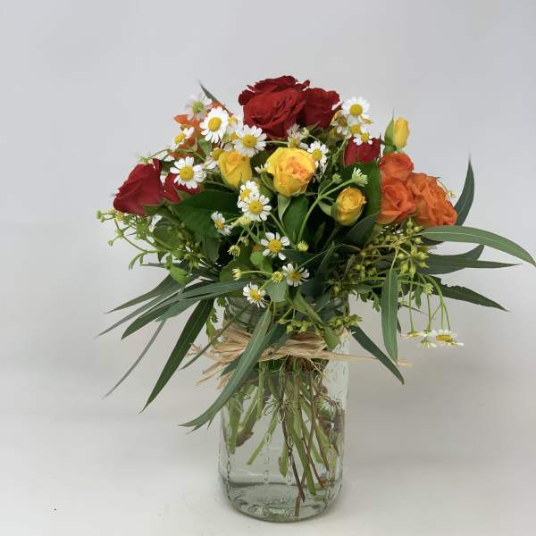Mixed bouquet of red and yellow roses with white daisies in a glass vase