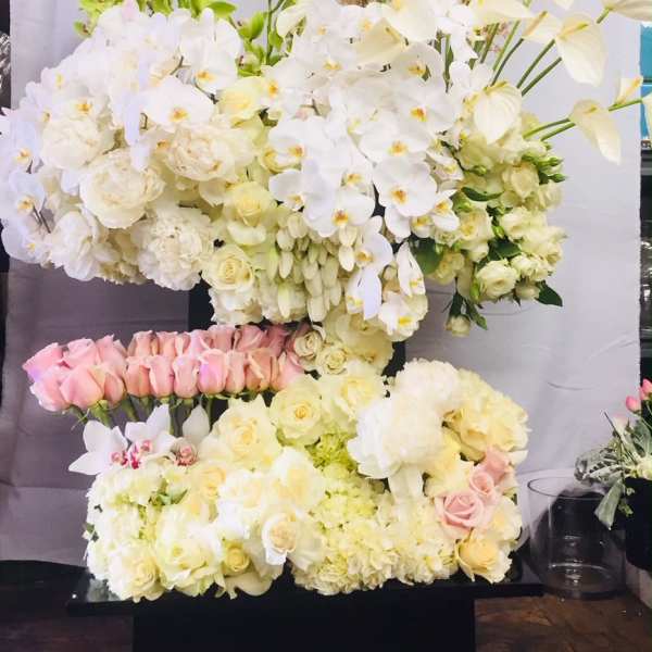 Large white floral arrangement with orchids and roses in a black container