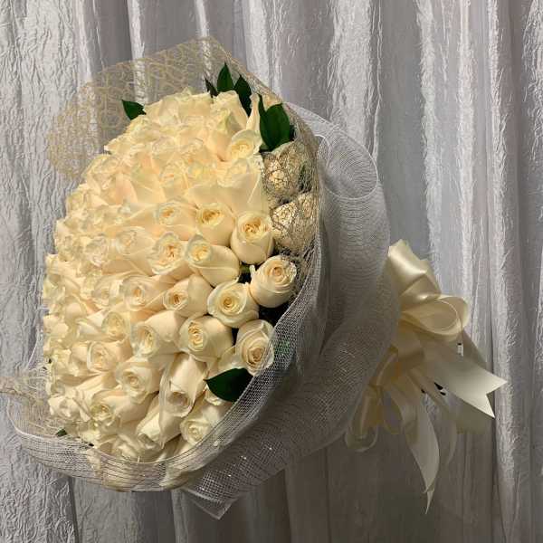 Large hand-tied bouquet of cream roses wrapped in white mesh with an ivory ribbon bow