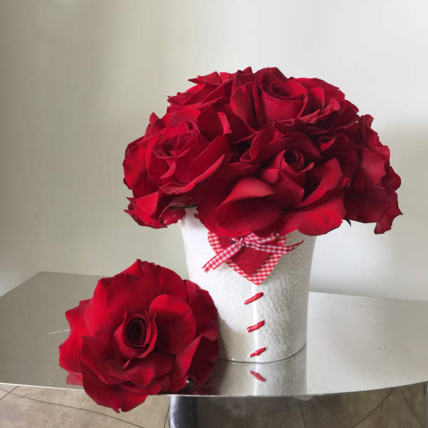 Red roses arranged in a white textured container with a gingham ribbon
