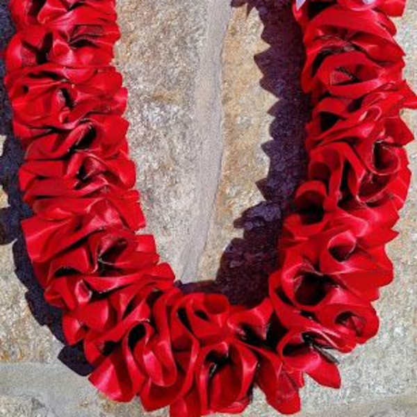 Red ribbon floral wreath with a white bow on a stone surface