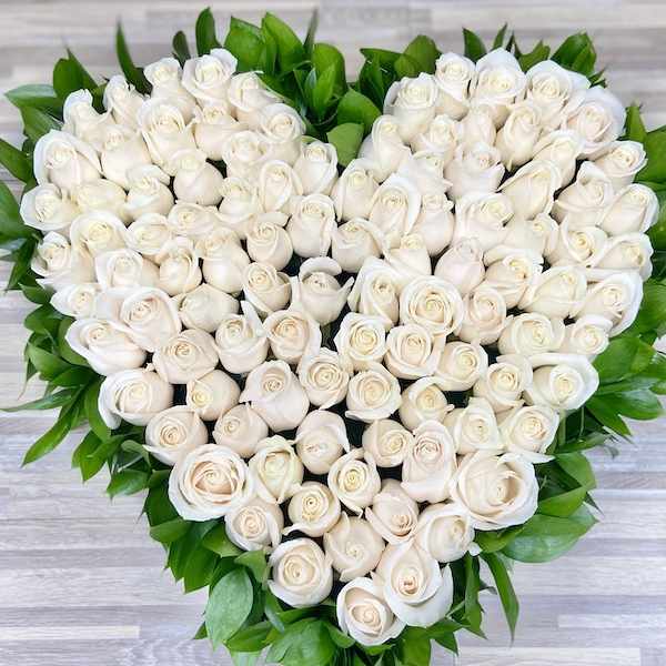 Heart-shaped arrangement of white roses edged with bright green foliage