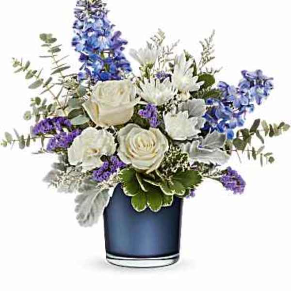 White roses and mums with blue delphinium and purple accents in a blue glass vase