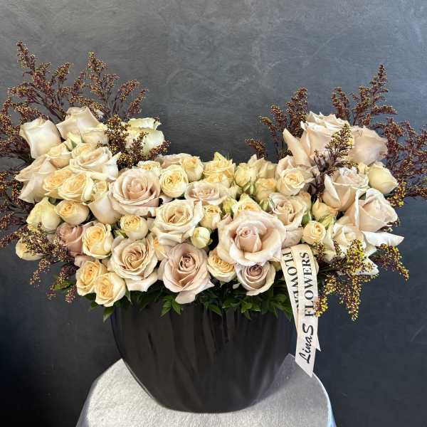 Large cream rose arrangement in a black vase with burgundy filler