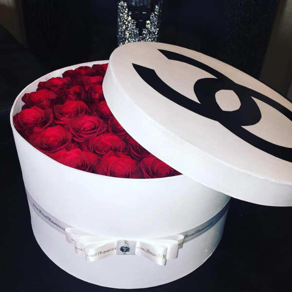 Round white box filled with red roses and a lid with a black logo