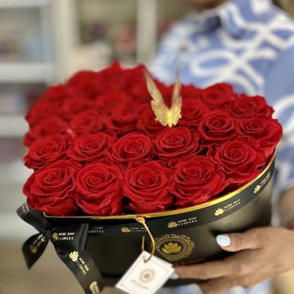 Heart-shaped black box filled with red roses and a gold butterfly accent, held in someone’s hands.