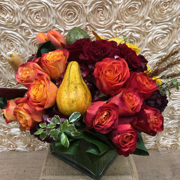 Bouquet of red and orange roses with decorative gourds in a vase
