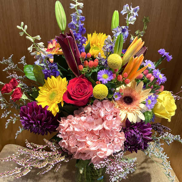 Colorful mixed bouquet in a glass vase with roses, lilies, and hydrangea