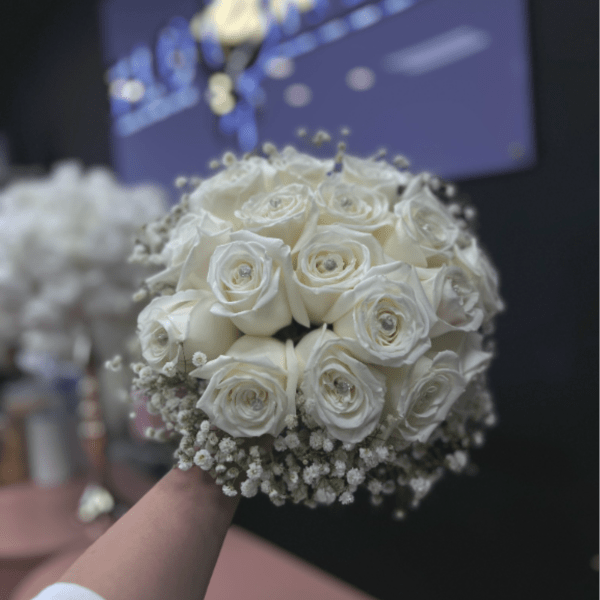 Round bridal bouquet of white roses and baby's breath held in front of a dark background