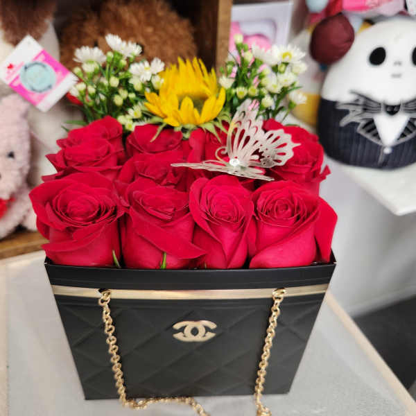 Black handbag-style box filled with red roses and small white flowers