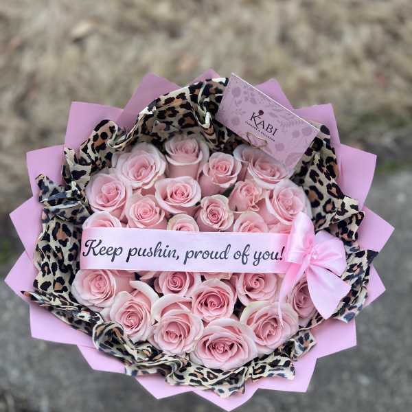 Pink rose bouquet wrapped in leopard-print paper with a ribbon banner