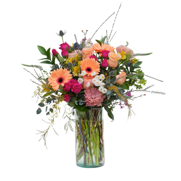 Tall mixed bouquet of peach gerbera daisies, roses, and assorted flowers in a clear glass cylinder vase
