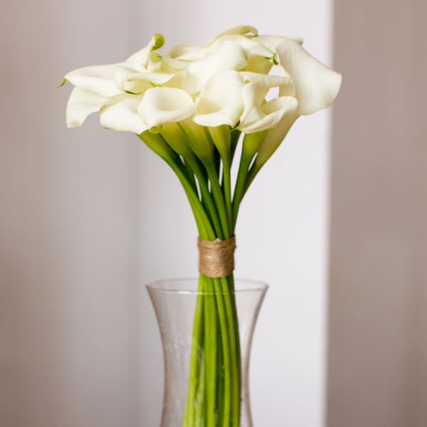 Tall bouquet of white calla lilies in a clear glass vase