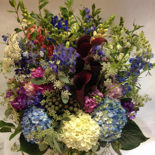 Mixed bouquet with hydrangeas, calla lilies, and delphinium in a glass vase
