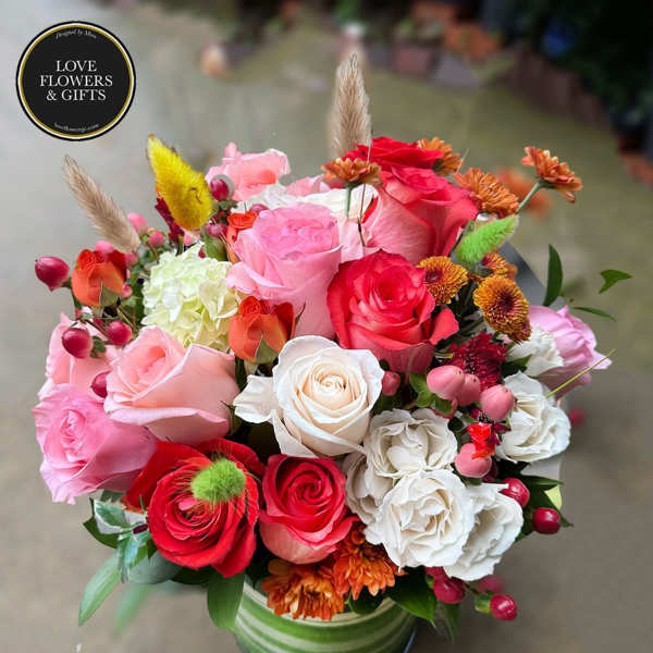Mixed arrangement of pink, red and white roses with accent blooms in a green striped vase
