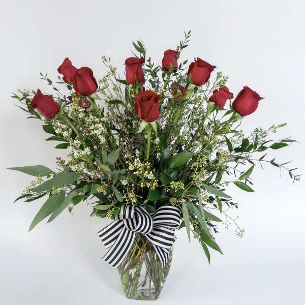Red roses in a clear glass vase with a black-and-white striped bow