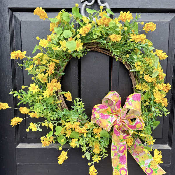 Yellow floral wreath with a pink patterned bow on a black door