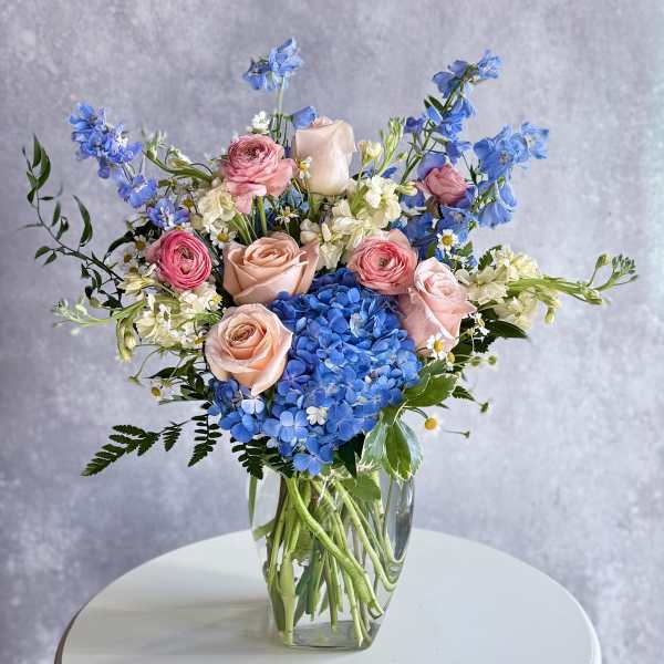Pink roses and blue hydrangeas arranged in a clear glass vase