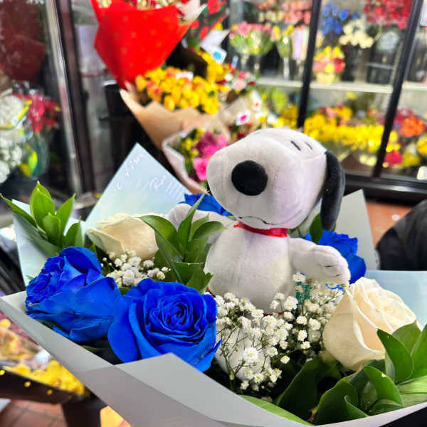 Bouquet of blue and white roses with baby's breath and a Snoopy plush toy wrapped in light paper