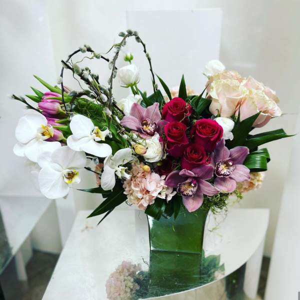Mixed bouquet of orchids, roses, and pale hydrangeas in a green vase