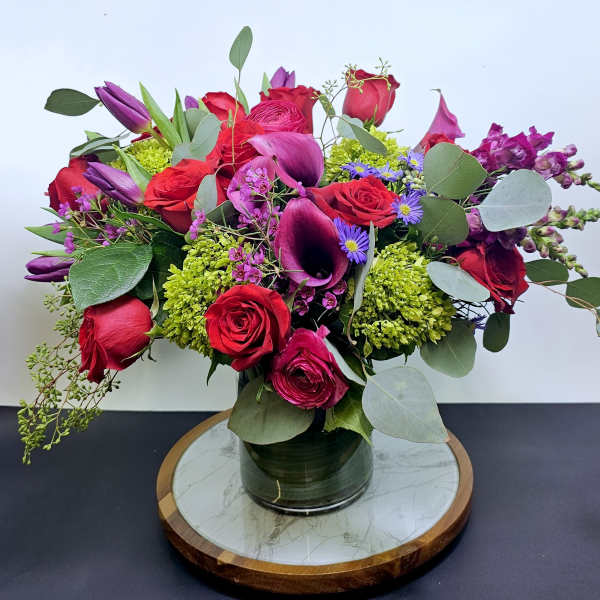 Bouquet of red roses, purple calla lilies, and green blooms in a glass vase