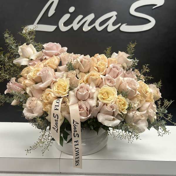 Large pastel rose arrangement in a white bowl vase with ribbon tags