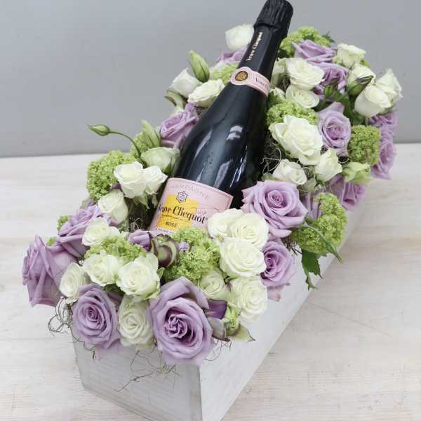 Rectangular box of lavender and white roses surrounding a rosé champagne bottle