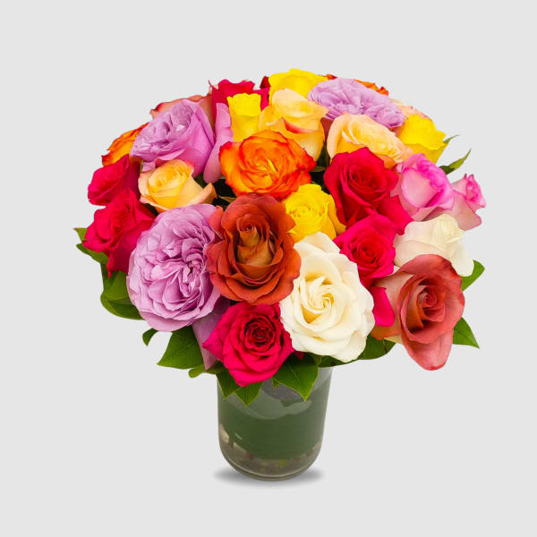 Mixed roses in bright pink, yellow, orange, and white in a glass vase