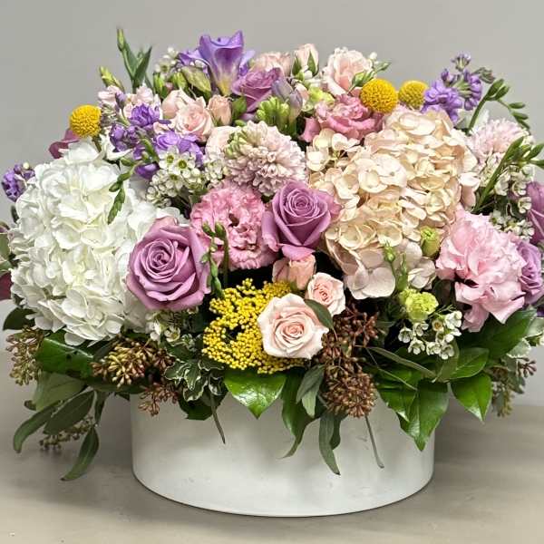 Low round arrangement of pink, lavender, white, and yellow flowers in a white container.