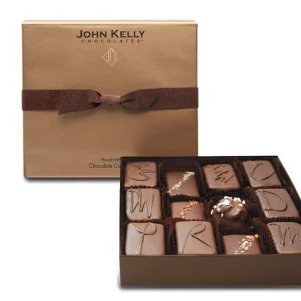 Square gold gift box with brown ribbon and assorted gourmet chocolates in an open tray.