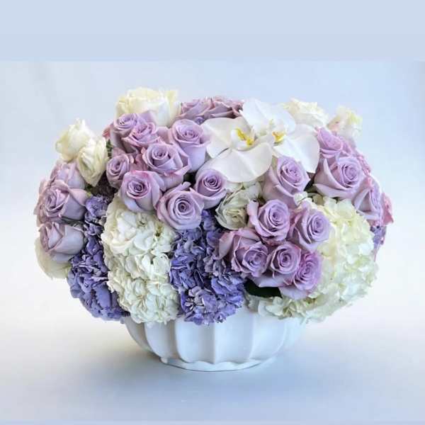 Lavender roses and white orchids arranged in a white vase
