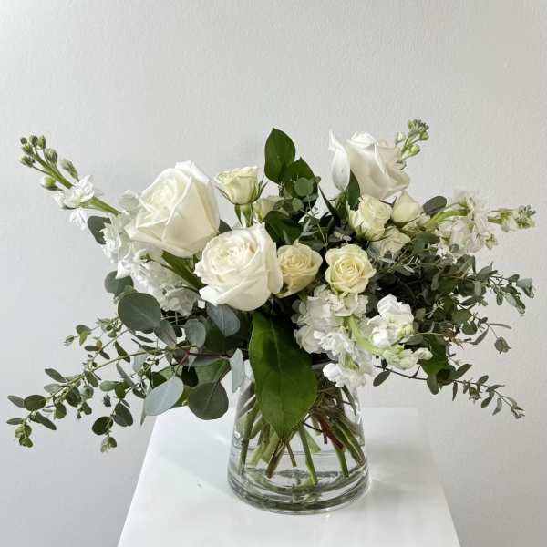 White roses and white blooms in a clear glass vase with greenery