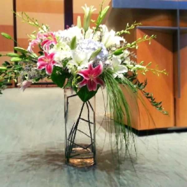 Tall floral arrangement with pink and white lilies in a metal stand