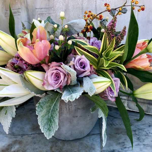 Low centerpiece of pink tulips, lavender roses, and white lilies in a gray pot