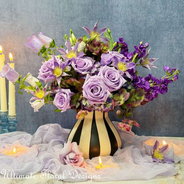 Lavender roses and purple flowers arranged in a striped vase with candles