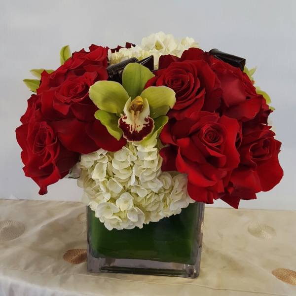 Red roses and white hydrangeas arranged in a square glass vase with a green orchid