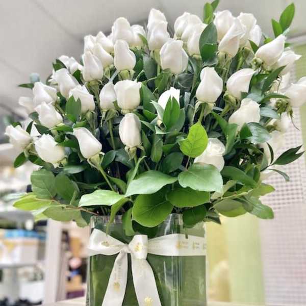 Arrangement of white rosebuds in a clear square vase with white ribbon