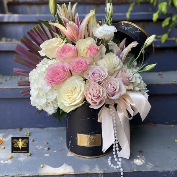 Round hat box arrangement of pink and white roses, lilies, and hydrangeas with ribbon and pearls