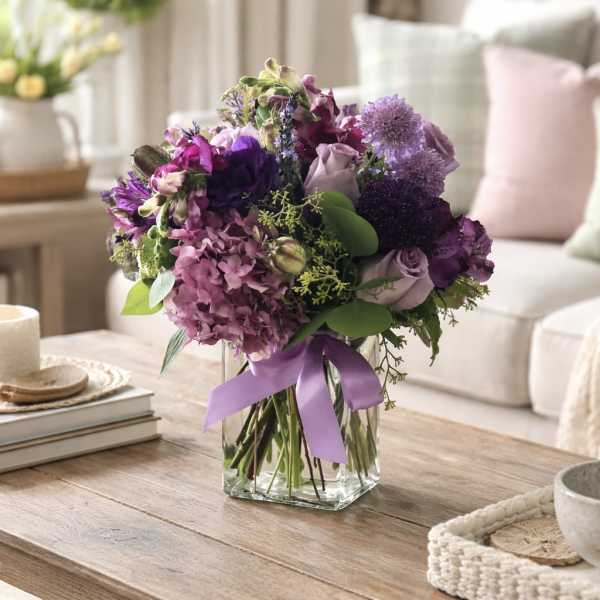 Purple bouquet in a clear glass vase with a lavender ribbon