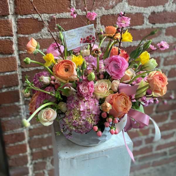 Colorful arrangement of roses, ranunculus, and hydrangeas in a white bowl with a birthday card