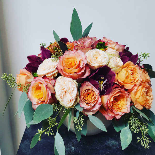 Bouquet of peach and white roses with dark purple flowers in a vase