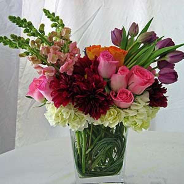 Mixed bouquet of pink roses, tulips, and burgundy blooms in a glass vase