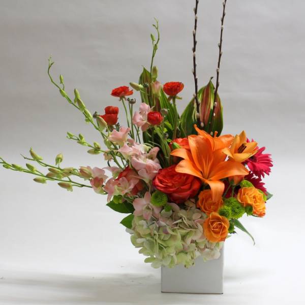 Colorful floral arrangement in a white rectangular vase with orange and pink blooms