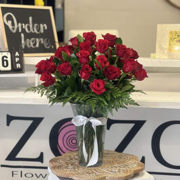 Tall bouquet of red roses in a clear glass vase with a white ribbon bow.