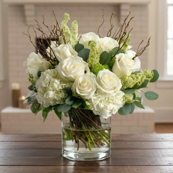 White roses and hydrangeas with branches in a clear glass cylinder vase