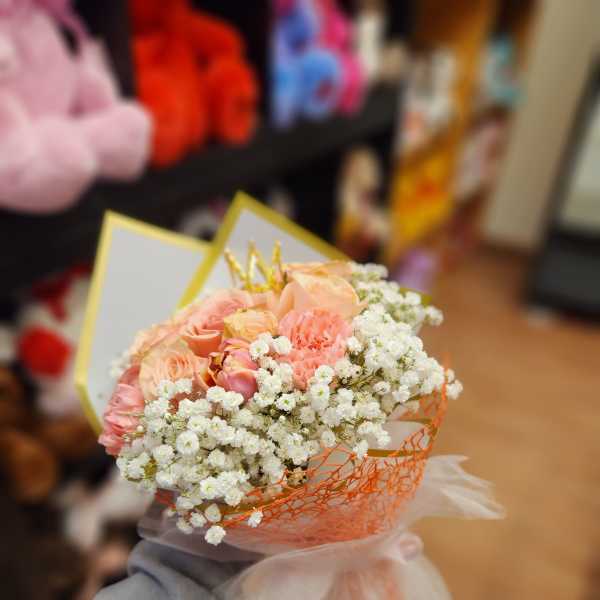 Handheld bouquet of peach roses and white baby's breath wrapped in orange mesh